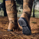 A close-up of a person's legs wearing brown suede boots stepping on pine needles.