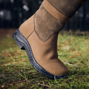 A close-up of a person's foot wearing a brown leather boot, stepping on grass.