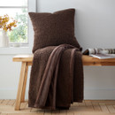 Chocolate brown blanket throw and pillow on a wooden bench near a window.