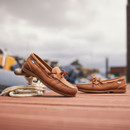 A pair of walnut brown deck shoes on a wooden pier. One of the shoes is leaning against a mooring point with rope coiled around it A pair of walnut brown deck shoes on a wooden pier. One of the shoes is leaning against a mooring point with rope coiled around it