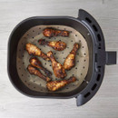 An air fryer basket with a liner inside with drumsticks on top