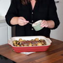 Person garnishing roasted potatoes in a red baking dish.