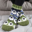 Someone with their feet crossed on a sofa stool wearing knitted socks with sheep on.