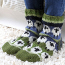 Someone with their feet on a fluffy rug wearing knitted socks with sheep on.