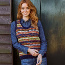 A woman standing outside by a door wearing a multicolour knit vest with a blue shirt underneath.