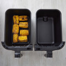 Grilled corn cobs in one side of a black, open, rectangular pan, other side empty, on a wood surface.