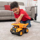 A child playing with a yellow and black JCB dump truck toy in front of a sofa.