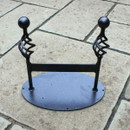 A small, ornate, black metal boot scraper on a stone pavement.