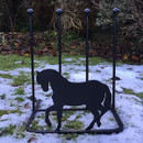 Metal horse silhouette boot rack on snowy ground with shrubbery background.