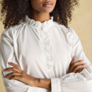 Close-up of a white frill-neck blouse highlighting the ruffled neckline and soft gathering around the shoulders.