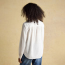 Back view of a woman in a white frill-neck blouse showing the gently gathered back yoke and loose silhouette, styled with blue jeans.