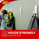 Three white utility hooks on a wall holding a bag and clothing, with a 3M Command brand logo.