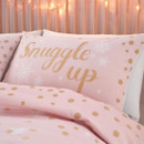 Cosy bed with pink, gold-accented "Snuggle up" pillow, dotted bedding, and warm lights.