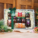 Gift hamper with jars of chutney and pickles, Scottish oatcakes, tied with a green bow. Festive background with pine branches, conveying a cosy holiday feel.