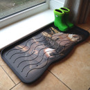 A pair of bright green rain boots sits on a black, wavy-patterned mat by a window on a tiled floor, creating a cosy, organized atmosphere.