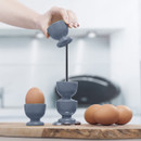 A hand placing a blue egg cup on top of a chrome stand.