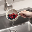 Hand washing berries in a colander over a kitchen sink.