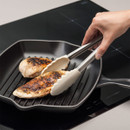 Hand using tongs to flip grilled chicken breasts in a grill pan on a stove.