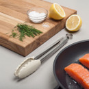Wooden cutting board with dill, salt, lemon, tongs, and salmon fillets in a pan.