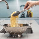 Hand lifting cooked spaghetti with tongs from a colander in a modern kitchen.