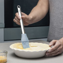Person using a silicone brush to apply egg wash on pastry in a white dish.