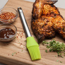 Grilled chicken on a cutting board with BBQ sauce, spices, and a basting brush.