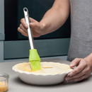 Person brushing egg wash onto pie crust in a baking dish with a silicone pastry brush.