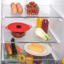 Open refrigerator with eggs, tomatoes, juice, pot with lid, fennel, carrots, zucchini, bell peppers, and corn.