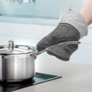 Hands in oven gloves lifting lid of a stainless steel pot on a stove.