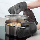 A person lifting a pot lid using oven gloves with cooking-related words on them.
