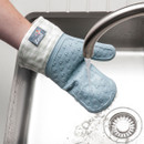 Person testing the water resistance of a blue silicone oven glove under a running tap.