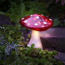 A red and white polka dot solar-powered mushroom light lit up in a garden