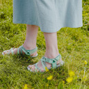 Person wearing green sandals and a blue skirt standing on grass.