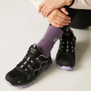 Black and purple walking shoes with breathable mesh uppers and lace-up fastening, worn with purple socks and black leggings in a seated pose.
