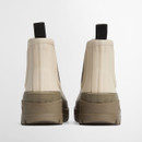 The back of a pair of short cream wellington boots with a dusky green chunky sole and black pull tabs.