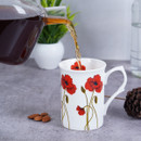 Pouring tea into a white mug with red flower design from a glass pot, with almonds on the table.