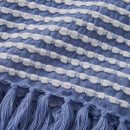 A close up view of a blue and white stab stitch design throw with frilled ends