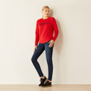 A person in a red jumper and blue jeans stands casually against a white wall, wearing black sneakers. The scene conveys a relaxed and stylish tone. A person in a red jumper and blue jeans stands casually against a white wall, wearing black sneakers. The scene conveys a relaxed and stylish tone.