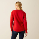 A person with blonde hair in a ponytail, wearing a red sweater and dark jeans, stands facing away against a light beige background. A person with blonde hair in a ponytail, wearing a red sweater and dark jeans, stands facing away against a light beige background.