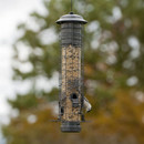 Bird feeder with a small bird, hanging against a blurred foliage background.
