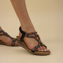 A person wearing decorative beaded sandals against a plain background.