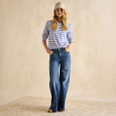 Woman wearing a blue-and-white striped long-sleeve T-shirt tucked into high-waisted wide-leg jeans, accessorised with a beige cap and boots.