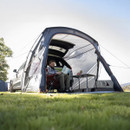 Person sitting in a chair by a car with attached tent, reading a map outdoors.
