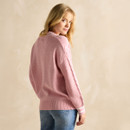 Person in a pink jumper and blue jeans against a beige background.