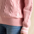 A pink cable-knit jumper with Joules branding detail on a person wearing blue jeans.