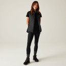 A full length view of a woman wearing a black quilted gilet over a short-sleeved t-shirt with leggings and walking boots.