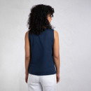 A woman with curly hair stands with her back to the camera, wearing a navy sleeveless top and white pants against a light background.