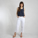 A woman stands confidently in a dark navy top and white wide-leg pants, paired with tan heeled sandals against a minimalist backdrop.