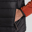 A hand in a black puffer gilet pocket with an orange sleeve visible. The textured fabric and zipper pull create a casual, cosy vibe.