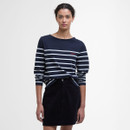 Woman in a navy and white striped top with a navy skirt stands against a plain background. She has a neutral expression and hands at her sides.